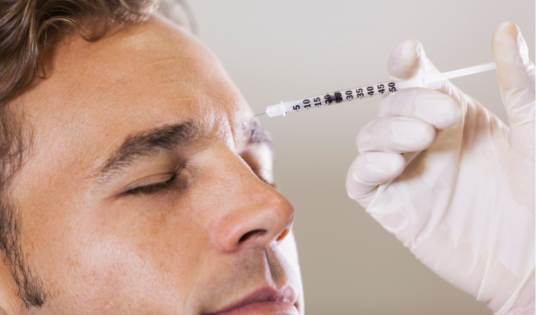 A white man with brown hair closes his eyes as he receives a neurotoxin injection in between his eyebrows.